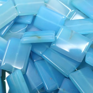 May include: A pile of light blue rectangular gemstone beads. The beads are smooth and polished, with a slight translucence.