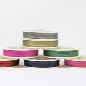 May include: Seven spools of wire in different colors, including gray, green, pink, and navy blue, are stacked on top of each other. The spools are all white and have a clear plastic cover.