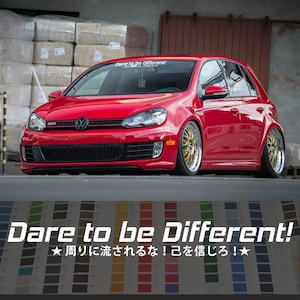 Puede incluir: Un Volkswagen GTI rojo con una pegatina "Dare to be Different!" en el parabrisas. El coche tiene detalles negros y llantas doradas. El texto "Dare to be Different!" también se muestra en letras grandes debajo del coche, junto con el texto "★周りに流されるな! 己を信じろ!★" en japonés.