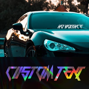 Puede incluir: Un coche negro con una calcomanía de vinilo iridiscente personalizada que dice "CUSTOM TEXT" en el parabrisas delantero. La calcomanía está en una fuente geométrica.