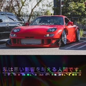 Peut inclure: Une voiture de sport rouge avec un autocollant noir et blanc qui dit "私は悪い影響を与える人間です。 BAD INFINITY" sur le pare-brise. La voiture a un pare-chocs avant noir et un aileron arrière noir.