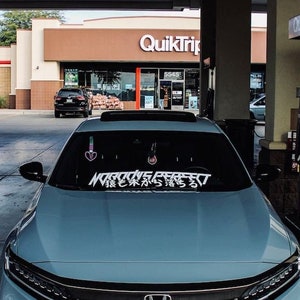 Könnte beinhalten: Ein hellblaues Auto mit einer schwarzen Windschutzscheibe und einem weißen Aufkleber auf der Windschutzscheibe, auf dem "MODIVE PERFECT" in Englisch und Japanisch steht. Das Auto steht an einer Tankstelle.