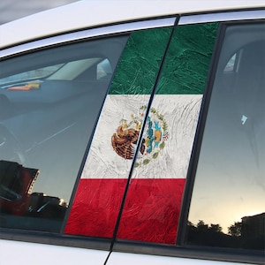 May include: Car window decals featuring the Mexican flag. The decals are rectangular and vertically oriented, with the flag's green, white, and red colors. The white section displays the Mexican coat of arms. The decals are affixed to a white car.