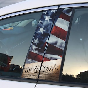 May include: A car window with a custom vinyl decal featuring an American flag and the text "We the People" from the US Constitution.
