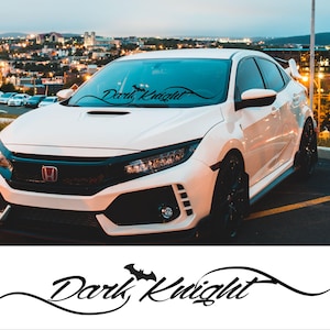 Pode incluir: Um Honda Civic branco com um adesivo preto "Dark Knight" no pára-brisa. O carro tem rodas pretas e um pára-choques dianteiro preto.