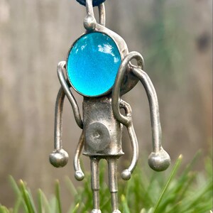 May include: A silver pendant necklace with a blue glass orb and a stylized figure design.