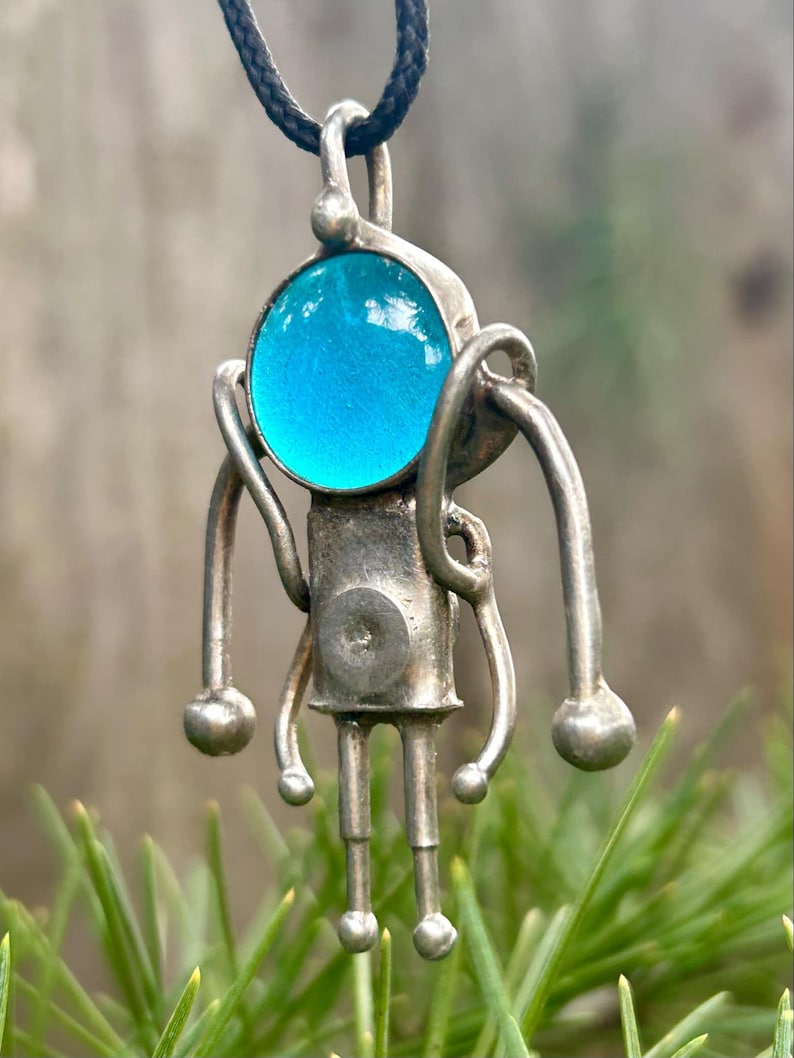 May include: A silver pendant necklace with a blue glass orb and a stylized figure design.