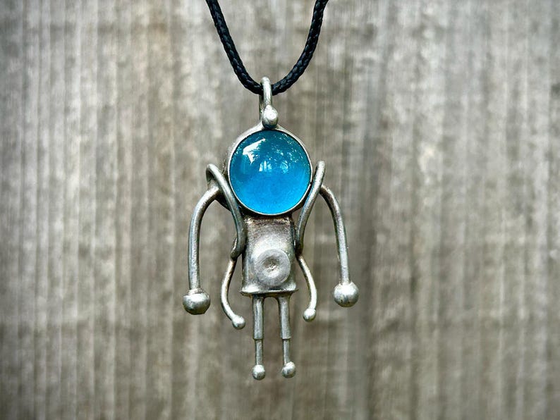 May include: A silver pendant necklace with a blue glass orb and a stylized figure design.