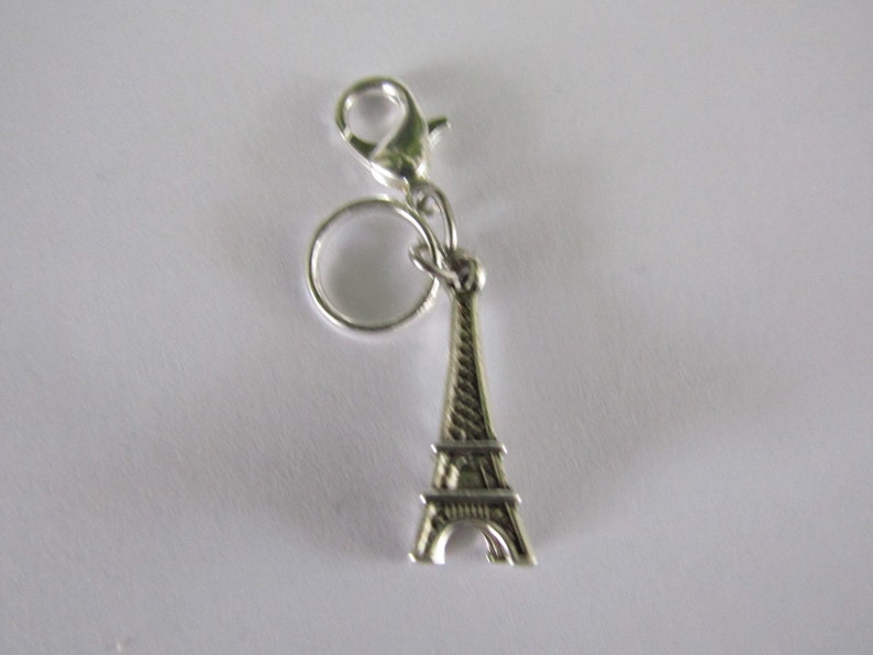 May include: Silver charm featuring a miniature Eiffel Tower with a silver ring and a lobster clasp.