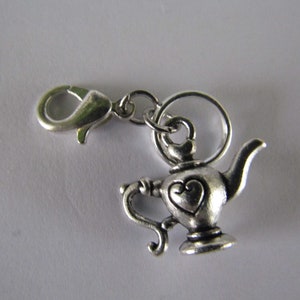 May include: Silver charm in the shape of a teapot with a heart design. The charm has a lobster clasp for attaching to a bracelet or necklace.