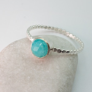 May include: A silver ring with a turquoise gemstone set in the center. The ring is made of small, round beads.