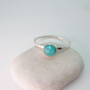 May include: A silver ring with a turquoise gemstone set in the center. The ring band is made of small silver beads.