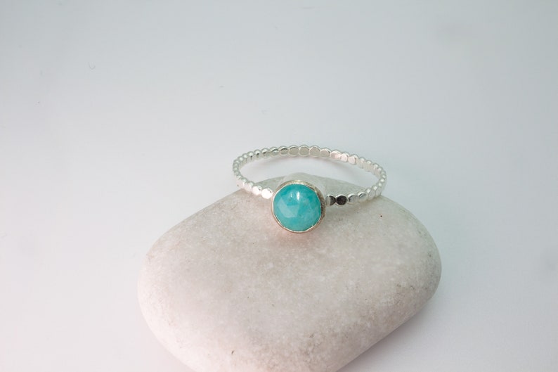 May include: A silver ring with a turquoise gemstone set in the center. The ring band is made of small silver beads.