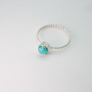 May include: A silver ring with a turquoise gemstone set in a bezel setting. The band is made of small silver beads.