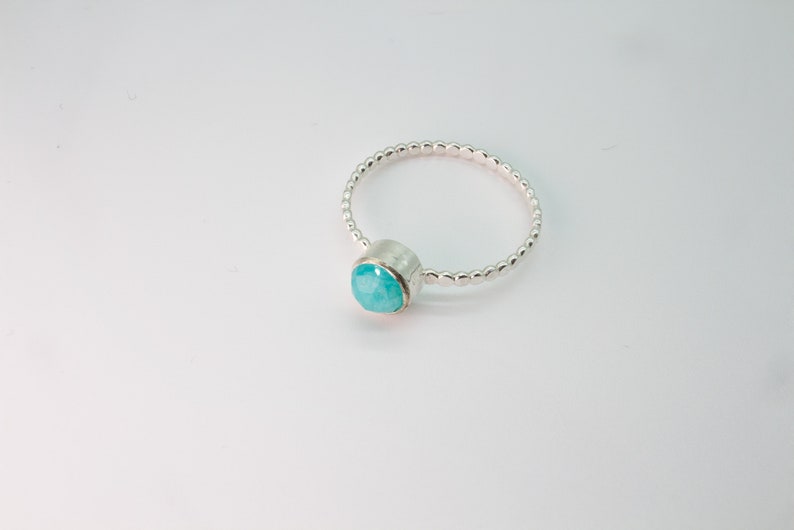 May include: A silver ring with a turquoise gemstone set in a bezel setting. The band is made of small silver beads.