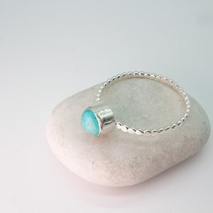 May include: A silver ring with a turquoise gemstone set in a bezel setting. The ring band is made of small, round beads.
