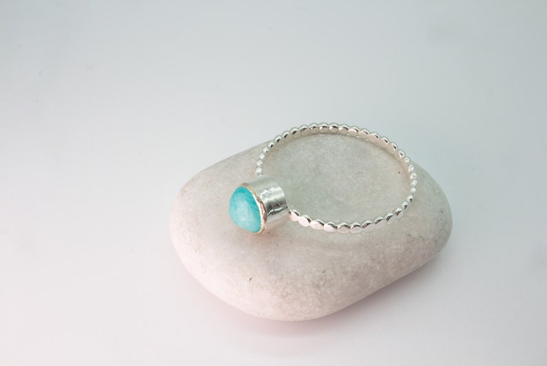 May include: A silver ring with a turquoise gemstone set in a bezel setting. The ring band is made of small, round beads.
