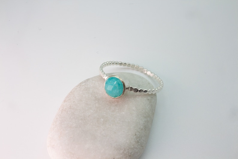 May include: A silver ring with a turquoise gemstone set in the center. The ring is made of small, round beads.