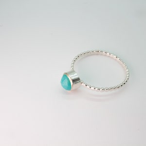 May include: A silver ring with a turquoise gemstone set in a bezel setting. The band is made of small, round beads.