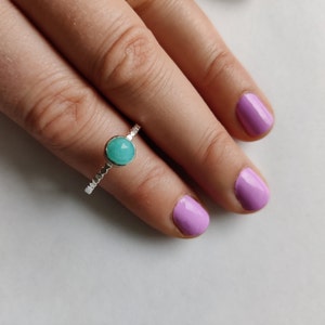 May include: A silver ring with a turquoise gemstone. The ring is on a finger with light pink nail polish.