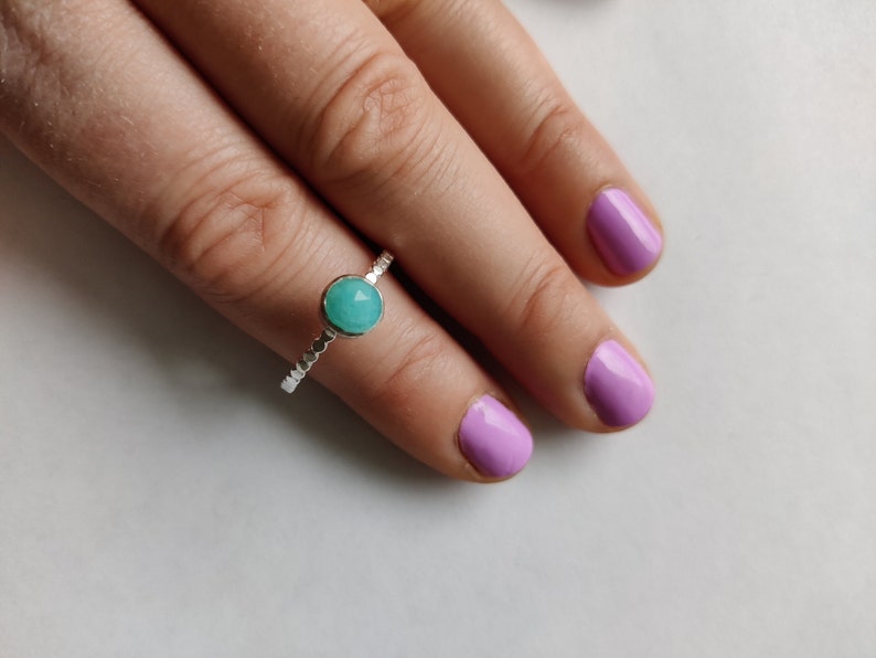 May include: A silver ring with a turquoise gemstone. The ring is on a finger with light pink nail polish.