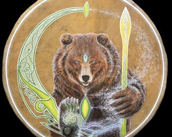 May include: A brown bear with a third eye is painted on a round, tan leather drum. The bear is holding a green staff with a yellow tip. The drum is decorated with green and white Celtic knotwork.