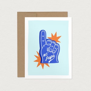 May include: A blue foam hand with the number one and the word "Papa" written on it. The hand is raised in the air with two orange starbursts behind it. The background is light blue.