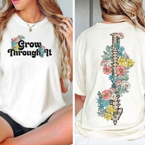 May include: White t-shirt with the text "Grow Through It" on the front and a floral design with a spine in the centre on the back.