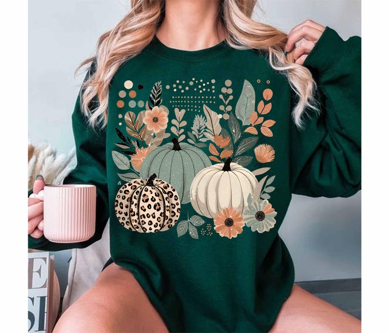 May include: A green sweatshirt featuring a graphic print of pumpkins and flowers. The pumpkins are in various shades of green, white, and brown with a leopard print pattern.