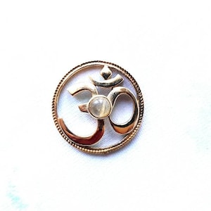May include: Gold-toned pendant featuring an Om symbol with a white gemstone in the center.