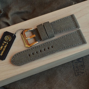 Puede incluir: Un cierre de reloj de lona verde con una hebilla dorada. La correa está hecha a mano en Italia y es 100% algodón.