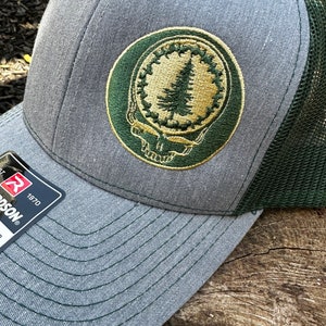 May include: Gray and green trucker hat with an embroidered patch featuring a tree and the words "grateful dead" in a circle.