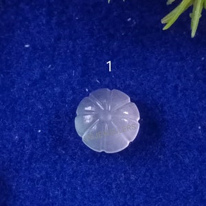 Puede incluir: Un cabuj&oacute;n blanco tallado en forma de flor, con un centro elevado y una superficie lisa y pulida.