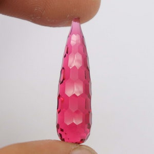 May include: A deep pink faceted gemstone in a teardrop shape. The gemstone has a hexagonal pattern.