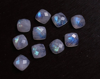 May include: A collection of ten iridescent moonstone gemstones, each cut into a square shape with rounded edges. The stones are arranged on a dark surface, showcasing their shimmering blue and white hues.