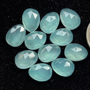 Może przedstawiać: Dziesięć fasetowanych, owalnych, jasnoniebieskich kamieni chalcedonowych. Kamienie są gładkie i wypolerowane.