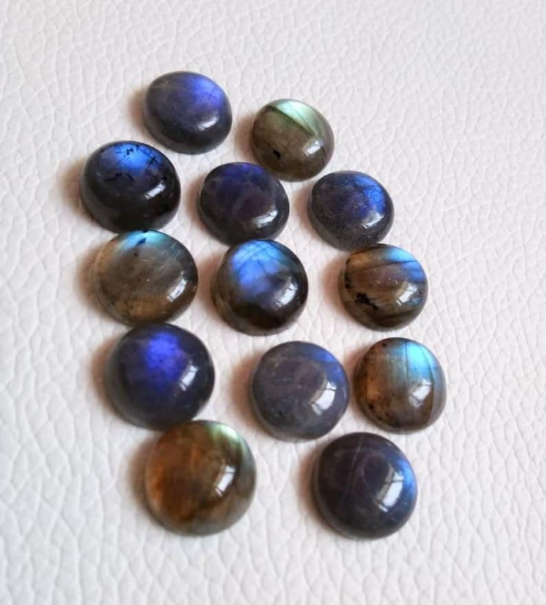 Pu&ograve; includere: Una collezione di 12 cabochon rotondi in labradorite iridescente. Le pietre sono un mix di colori blu, verdi e marroni con una finitura iridescente scintillante.