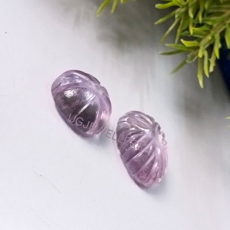K&ouml;nnte beinhalten: Zwei ovale, geschnitzte Edelsteine in Lavendel- und Lilat&ouml;nen. Die Edelsteine sind mit einem blattartigen Muster mit detaillierten Adern versehen. Sie liegen auf einer wei&szlig;en Oberfl&auml;che, mit einem Hauch von Gr&uuml;n im Hintergrund.