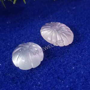 Puede incluir: Dos piedras preciosas blancas talladas en cabuj&oacute;n con un dise&ntilde;o floral. Las piedras preciosas est&aacute;n sobre un fondo azul.