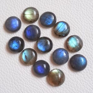 Pu&ograve; includere: Una collezione di 14 cabochon rotondi in labradorite iridescente in tonalit&agrave; di blu, verde e grigio. Le pietre sono lisce e lucidate, con una variet&agrave; di motivi e texture.