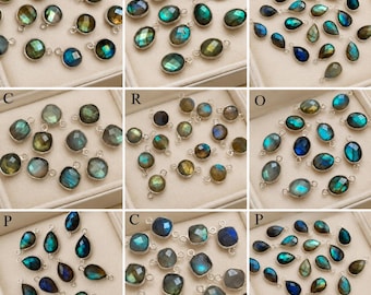 May include: A collection of labradorite gemstone charms set in silver-toned metal frames. The charms feature various shapes including round, oval, pear, and square, displaying iridescent flashes of blue, green, and gold colors across the surfaces.