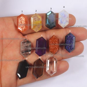 Puede incluir: Once cabujones de piedras preciosas facetados en varios colores y formas, incluyendo piedra de sol, amatista, labradorita, piedra lunar, obsidiana negra, cuarzo ahumado y cuarzo transparente. Las piedras preciosas están dispuestas en filas en una mano.