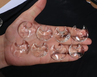 May include: Eight clear glass crescent moon shaped pendants with the text "UNITEDGEMSEWELLERS" on each.