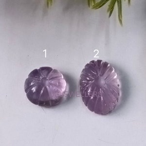 K&ouml;nnte beinhalten: Zwei geschnitzte Amethyst-Edelsteine. Einer ist rund, &auml;hnelt einem K&uuml;rbis, der andere ist oval. Beide haben detaillierte, geschnitzte Rippen, die von einem zentralen Punkt ausgehen. Die Edelsteine haben eine durchscheinende violette Farbe.