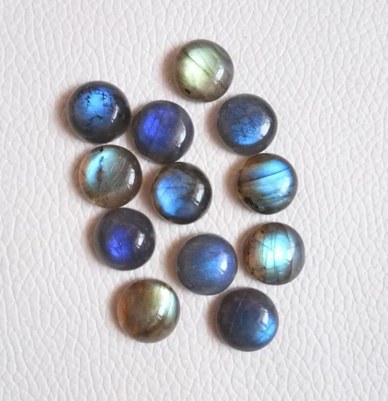 Pu&ograve; includere: Una collezione di 12 cabochon rotondi in labradorite iridescente in tonalit&agrave; di blu, verde e oro. I cabochon sono lisci e lucidi, con una variet&agrave; di motivi e texture.