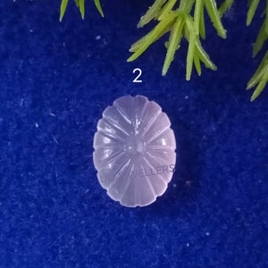 Puede incluir: Primer plano de un cabuj&oacute;n blanco de forma ovalada con un dise&ntilde;o tallado en forma de sol. El cabuj&oacute;n est&aacute; sobre un fondo azul.