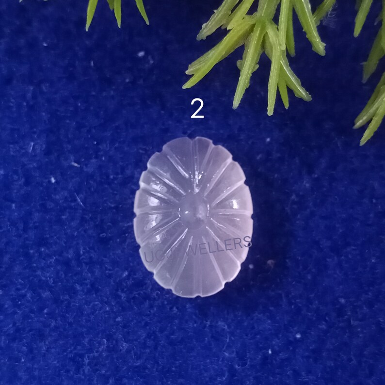 Puede incluir: Primer plano de un cabuj&oacute;n blanco de forma ovalada con un dise&ntilde;o tallado en forma de sol. El cabuj&oacute;n est&aacute; sobre un fondo azul.