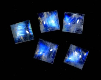 May include: Five square-shaped moonstone cabochons with a blue iridescent sheen. The stones are arranged in a semi-circle on a black background.