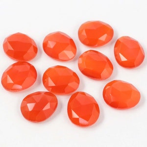Może przedstawiać: Dziesięć pomarańczowych kaboszonów z karneolu, każdy o fasetowanym owalnym kształcie. Kamienie są ułożone w luźny skupisko na białym tle.