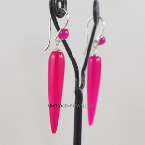 Può includere: Un paio di orecchini pendenti in pietra rosa con ganci d'argento. Le pietre preziose sono lunghe e appuntite, con una pietra rotonda più piccola nella parte superiore di ogni orecchino.